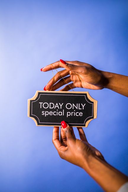 A pair of hands with red-painted nails holding a small black sign with a gold border that reads 'TODAY ONLY special price' against a plain blue background. The hands are positioned with one supporting
