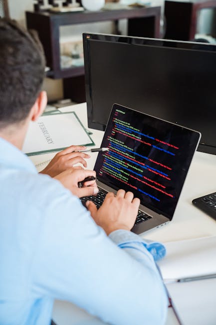 A close-up view of an open laptop on a dark surface, displaying lines of code on its screen with a blurred background. Next to the laptop, there is a white baseball cap with the Puma logo on the front